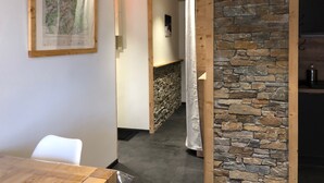 A room with a wooden ceiling, a stone wall, a white chair, and a framed map on the wall. - BEAUTIFUL T3 ESPRIT CHALET (LES ANGLES)