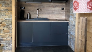 A compact kitchen with dark cabinets, a wooden countertop, and a stone wall. - BEAUTIFUL T3 ESPRIT CHALET (LES ANGLES)