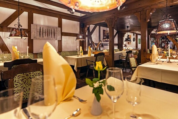 A restaurant interior with wooden beams, tables set with yellow napkins, and hanging lanterns.