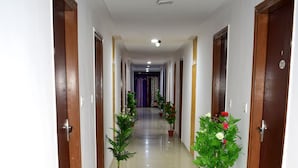 A hotel hallway with wooden doors, potted plants, and a tiled floor. - Hotel Radhe (Vadodara)