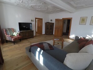 Een woonkamer met een bank, fauteuil, televisie, houten kast en een bijzettafeltje.