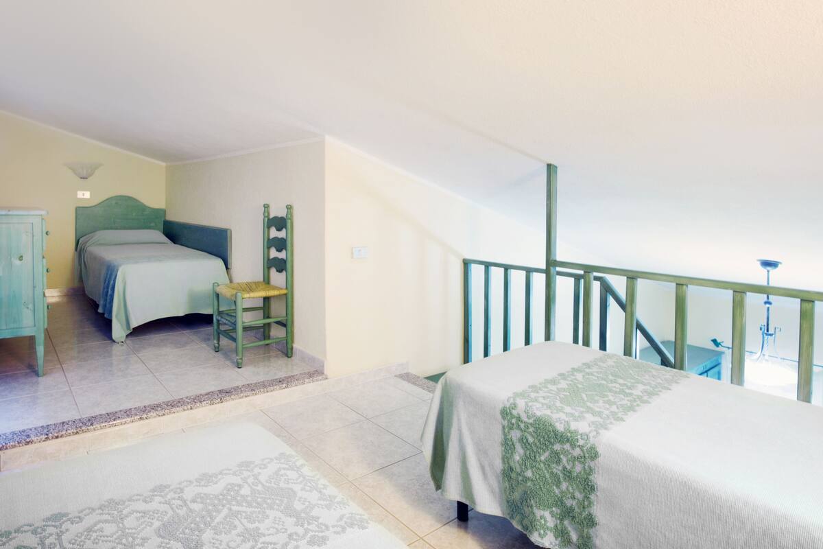 A bedroom with a bed, a chair, a dresser, and a staircase.