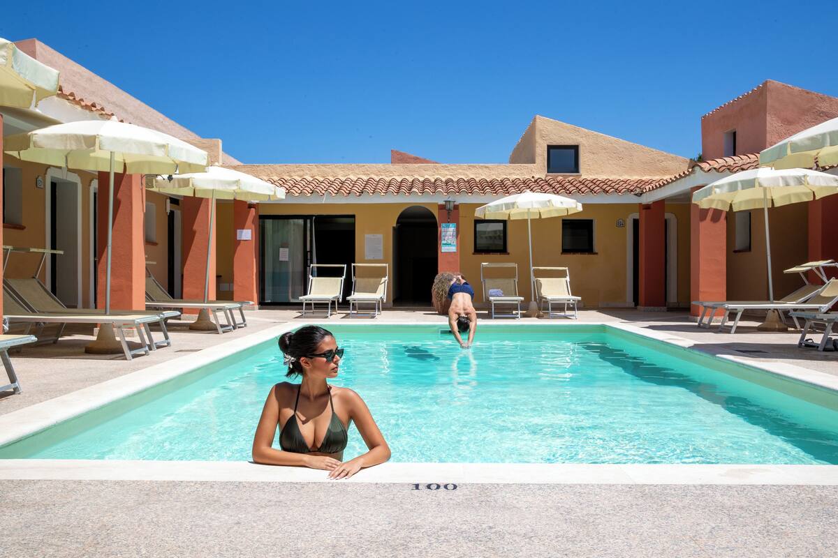 A swimming pool with sun umbrellas, lounge chairs, and a building with a tiled roof.
