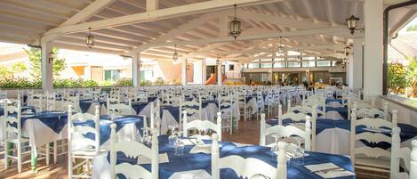 A large indoor dining area with white and blue tablecloths, white chairs, and hanging lanterns.