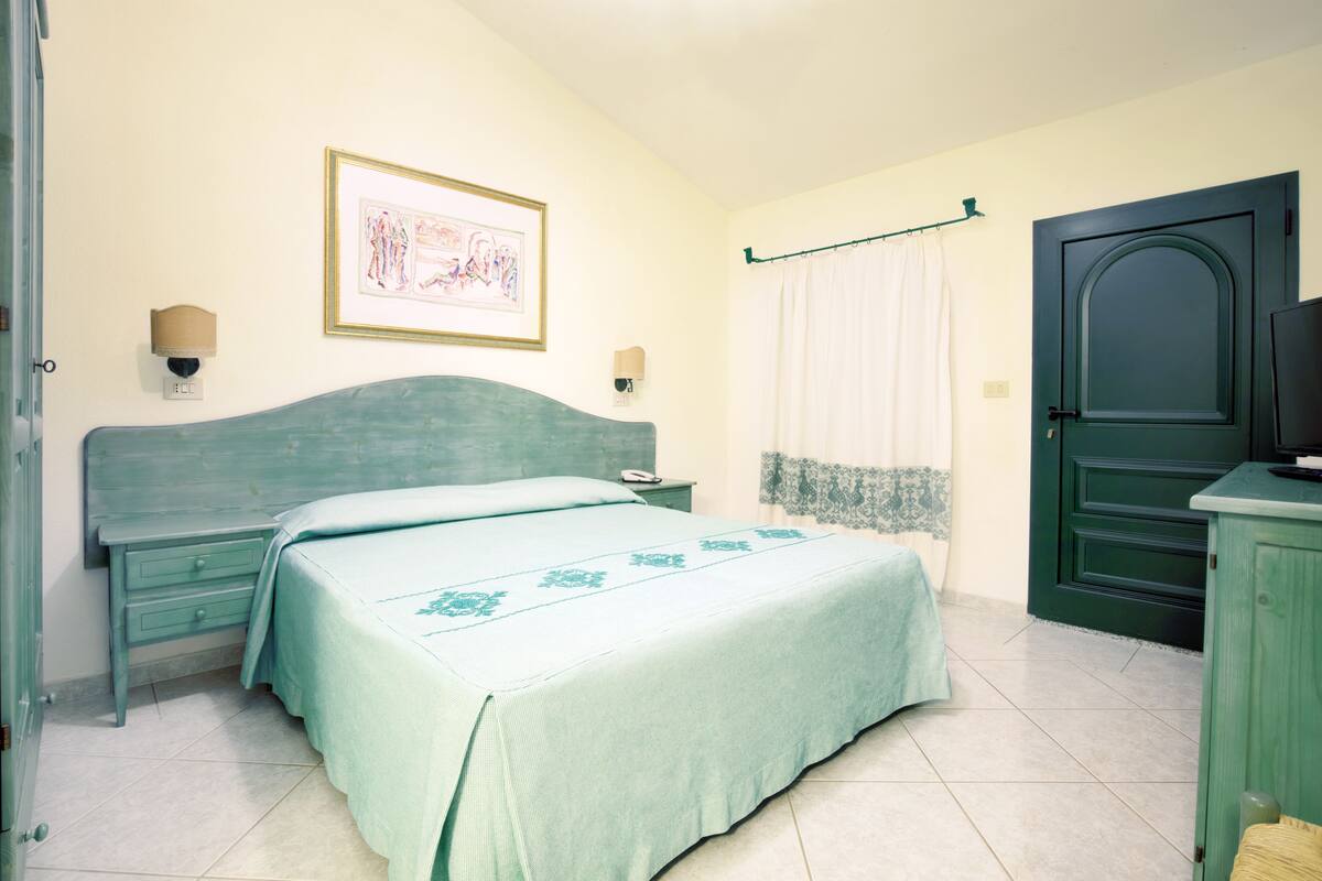 A bedroom with a bed, a nightstand, a dresser, a door, and a wall-mounted light fixture.
