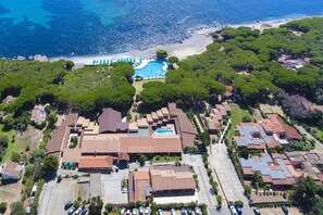 An aerial view of a resort with a swimming pool surrounded by lush greenery, a beach, and a parking area. - Club Hotel Marina Seada Beach (Budoni)