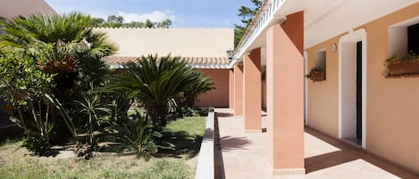 A corridor with a tiled floor, palm trees, and a building with a beige facade and white trim.