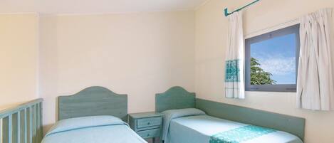A bedroom with two single beds, a nightstand, a window with curtains, and a view of the sky.
