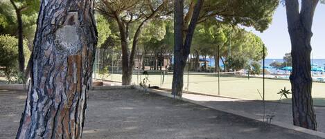 Un parque con árboles, una zona vallada y vistas al mar.