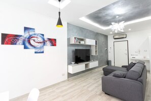 Un salon moderne avec un canapé gris, un téléviseur à écran plat, des étagères blanches intégrées et des œuvres d’art abstraites accrochées au mur.