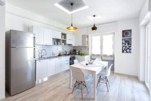 Une cuisine moderne avec des meubles blancs, des appareils en acier inoxydable et un coin repas comprenant une table et des chaises blanches.