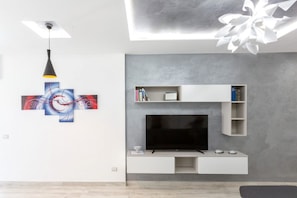 Una sala de estar moderna con un televisor de pantalla plana, estanterías empotradas blancas y una lámpara de techo.