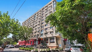 Un immeuble à plusieurs étages doté de balcons, d’une devanture rouge et de voitures garées.