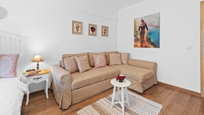 Un salon moderne avec un canapé beige, une petite table blanche surmontée d’une lampe et un tableau accroché au mur.