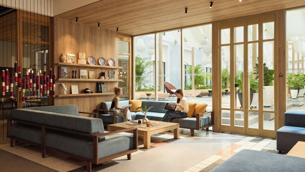 Un hall d’hôtel moderne avec un plafond en bois, de grandes fenêtres et un espace détente comprenant des canapés et une table basse.