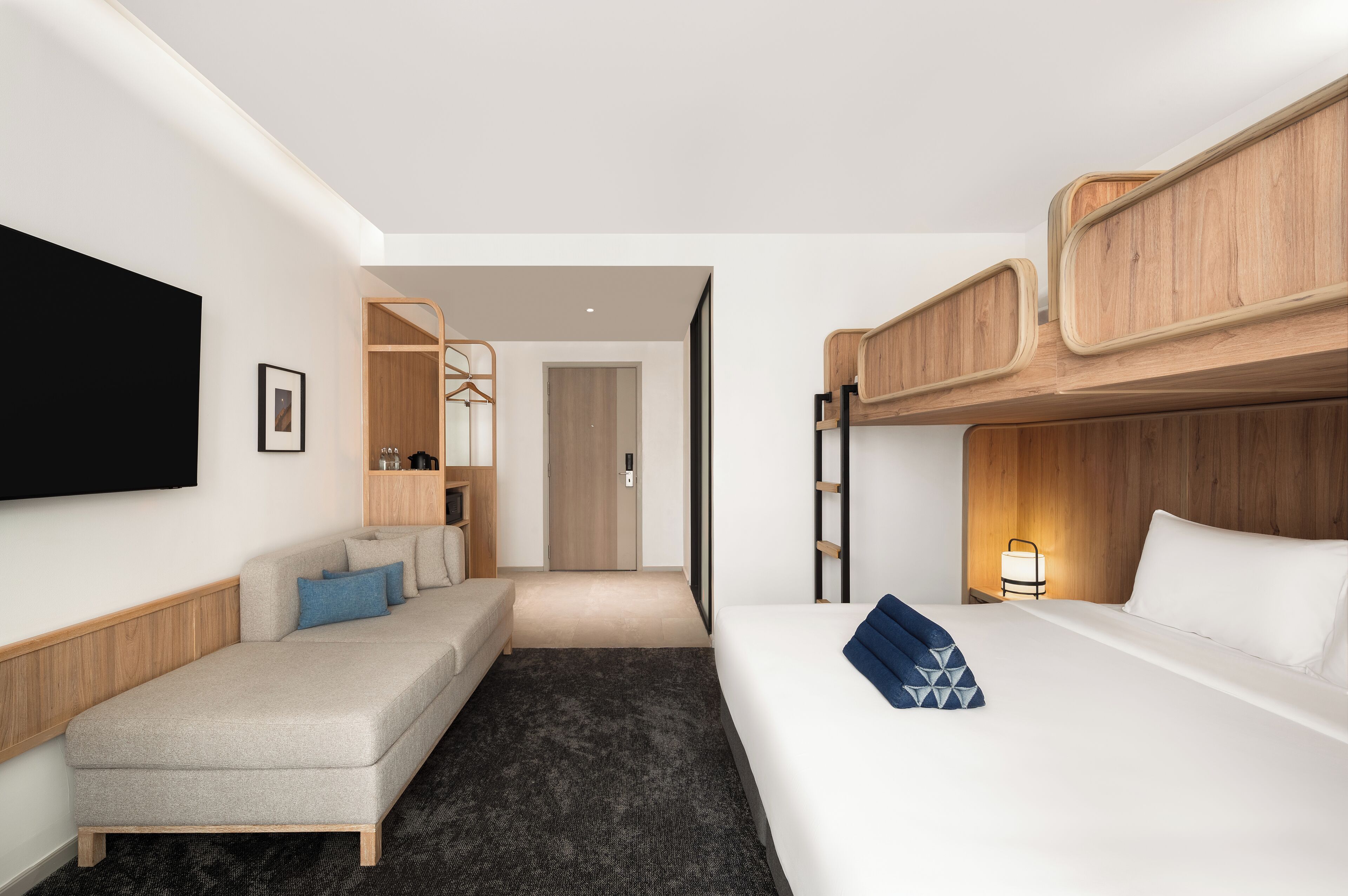 A hotel room with a sofa, a bed, a TV, a wooden headboard, and a door leading to another room.