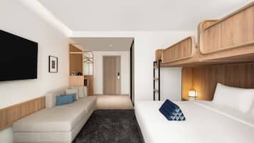 A hotel room with a sofa, a bed, a TV, a wooden headboard, and a door leading to another room.