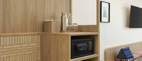 Habitación de hotel con un armario de madera, un minibar negro, un banco de madera y un televisor montado en la pared.
