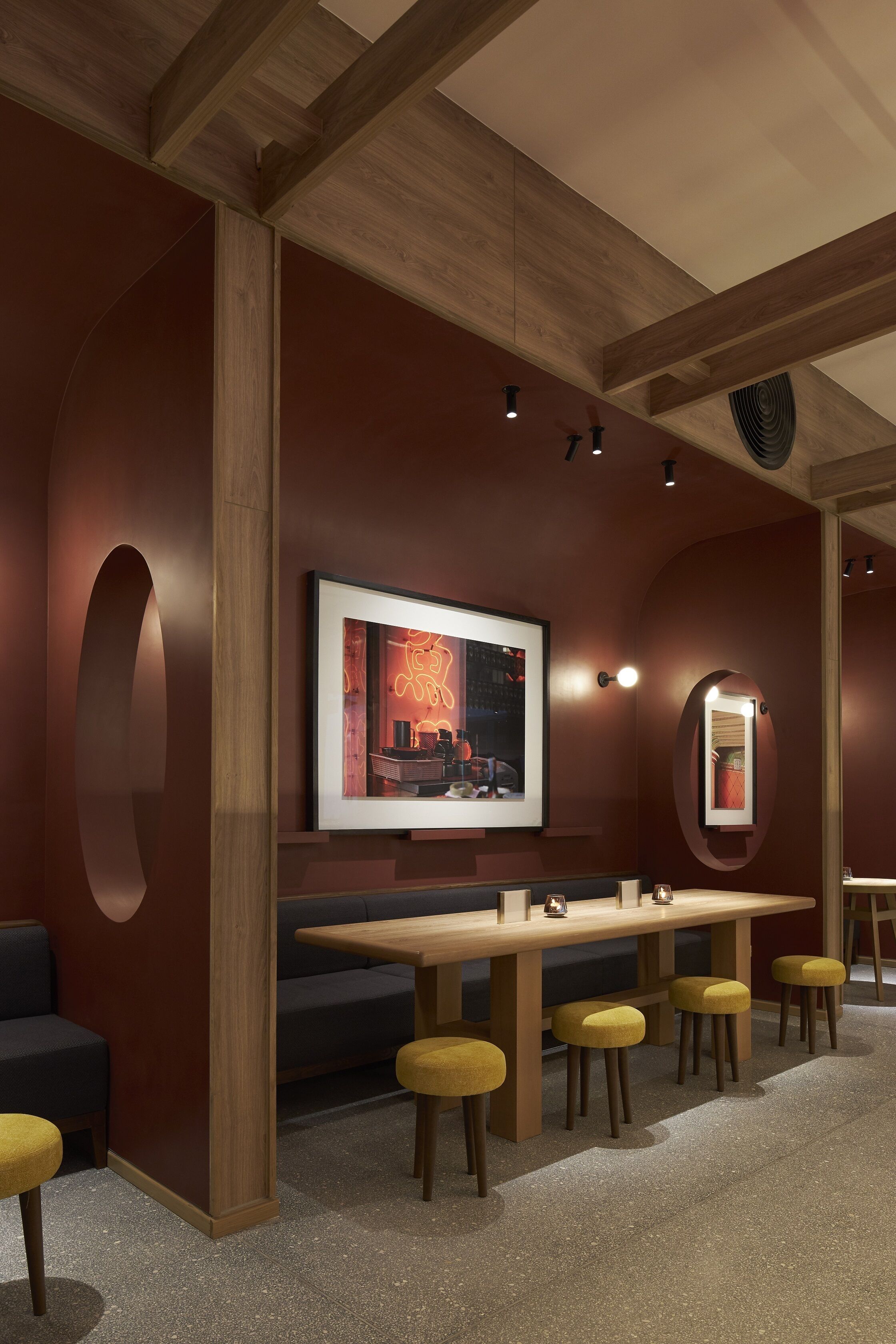 A modern interior with a wooden ceiling, a long table with yellow stools, and a framed picture on the wall.