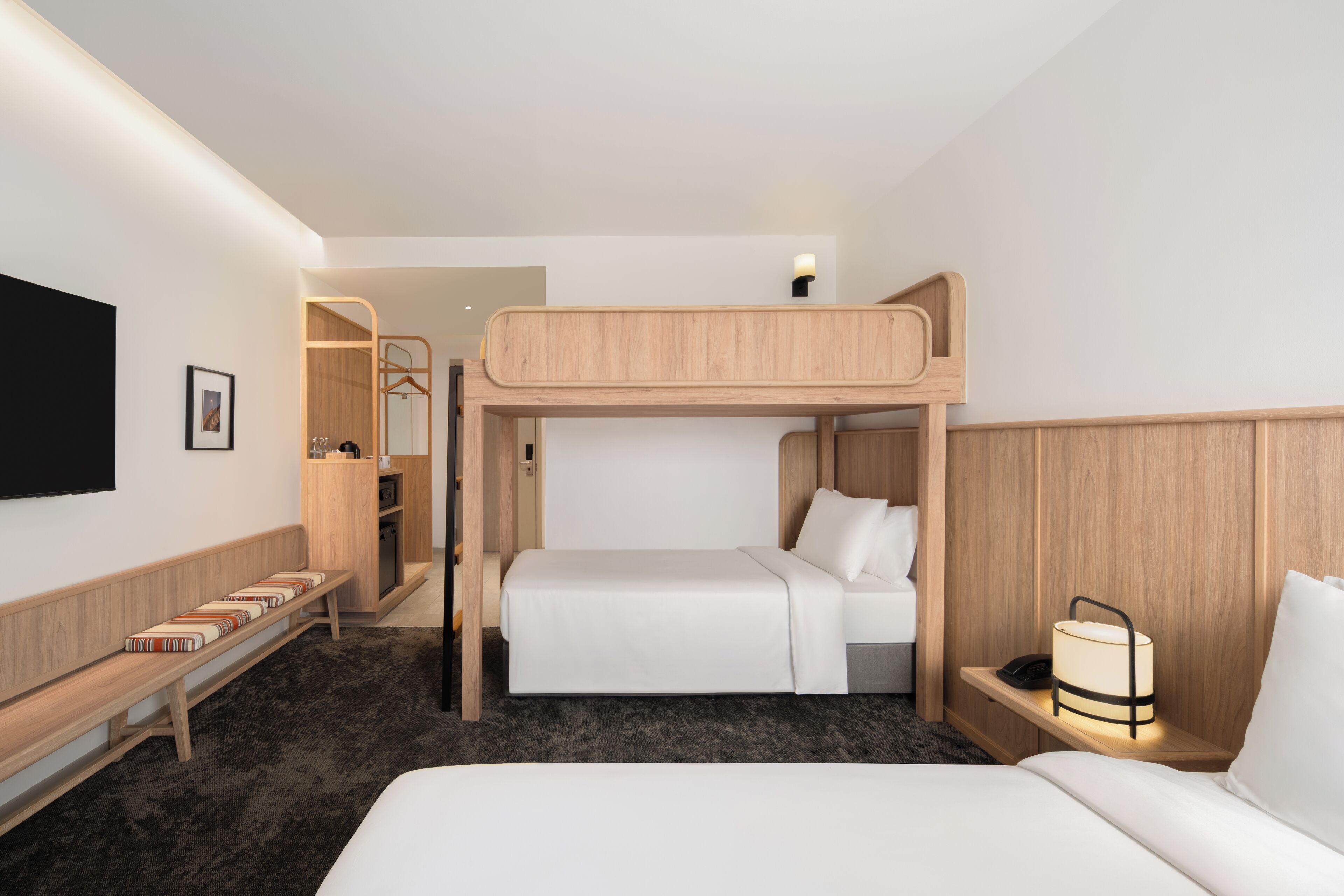 A bunk bed room with a desk, a bedside lamp, and a TV mounted on the wall.