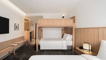 A bunk bed room with a desk, a bedside lamp, and a TV mounted on the wall.