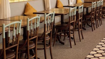 A restaurant with wooden tables and chairs, white curtains, and hanging pendant lights.
