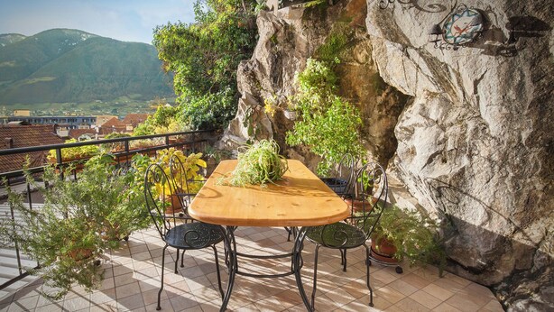 A balcony with a wooden table and chairs, surrounded by potted plants and a view of a mountainous landscape. - Casa Al Duomo-Apartment in the historic center of Merano (Merano)