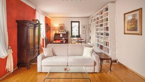 A living room with a white sofa, a wooden cabinet, a piano, and a bookshelf. - Casa Al Duomo-Apartment in the historic center of Merano (Merano)