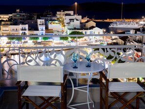 A balcony with white chairs and a table, overlooking a marina with boats and a cityscape at night. - Emerald  Top studio, overlooking the picturesque lake Voulismeni (Ag. Nikolaos)