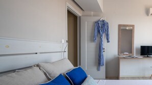 Un dormitorio con cama, almohadas, una bata colgada en la puerta, un escritorio con computadora y un espejo.