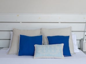 A bed with a white headboard and three pillows in different shades of blue and beige.
