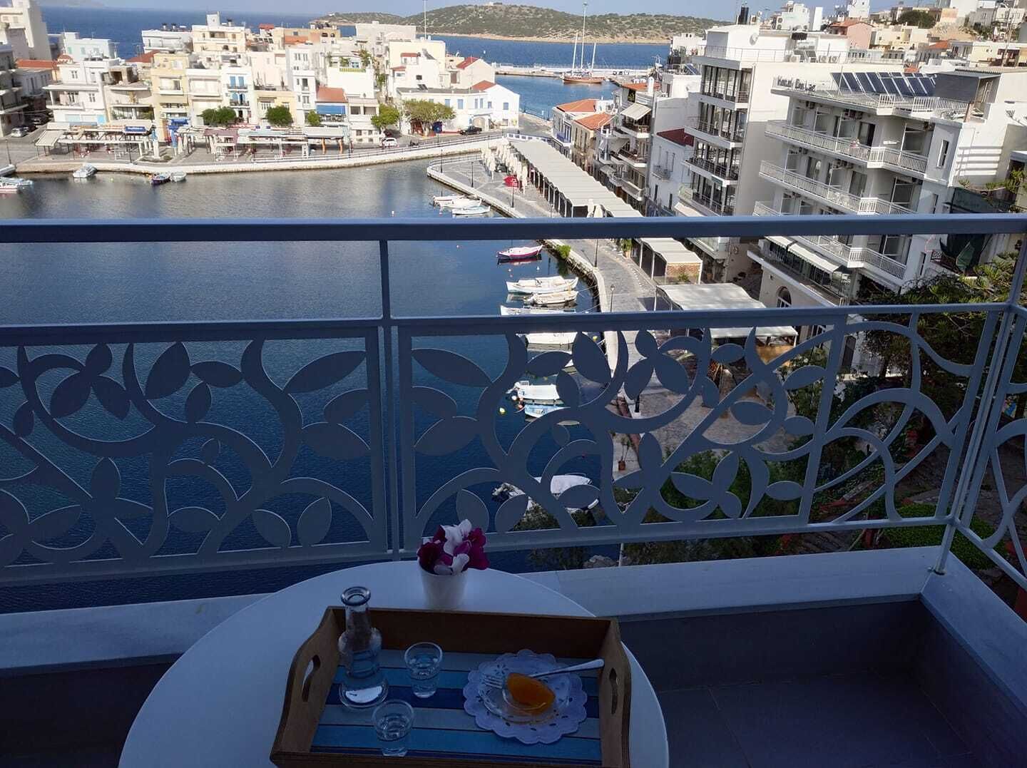 Un balcón con vistas al puerto, que presenta una barandilla decorativa y una mesa con una bandeja de vasos y una botella.