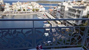 Un balcón con vistas al puerto, que presenta una barandilla decorativa y una mesa con una bandeja de vasos y una botella.
