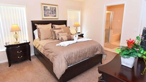 A bedroom with a large bed, two bedside tables with lamps, a framed picture on the wall, and a potted plant on a side table. - Malaki (Davenport)