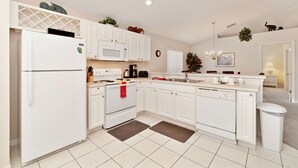 A modern kitchen with white cabinetry, a built-in oven, a microwave, and a sink. There are decorative plants and a chandelier. - Malaki (Davenport)