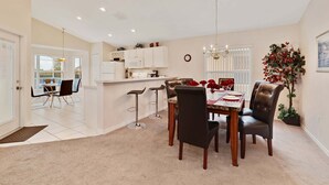 A dining area with a table set for four, surrounded by chairs, a kitchen in the background, and a large potted plant. - Malaki (Davenport)