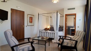 Un dormitorio con cama con dosel, una mesita de noche, una silla, un sofá, un televisor y una puerta.