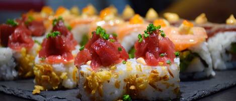 Sushi rolls with toppings on a slate serving board.