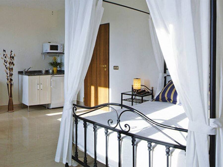 Ein Schlafzimmer mit Bett, Nachttisch, Lampe, Stuhl, Schreibtisch, einem kleinen Tisch, einem Schrank und einem Fenster mit Vorhängen.