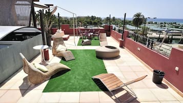 A rooftop terrace with wicker lounge chairs, a round seating area, and a view of the ocean.