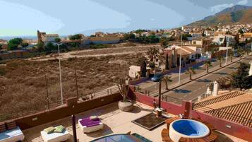 Un área de piscina en la azotea con sillones de descanso, un jacuzzi y vistas a un pueblo costero.