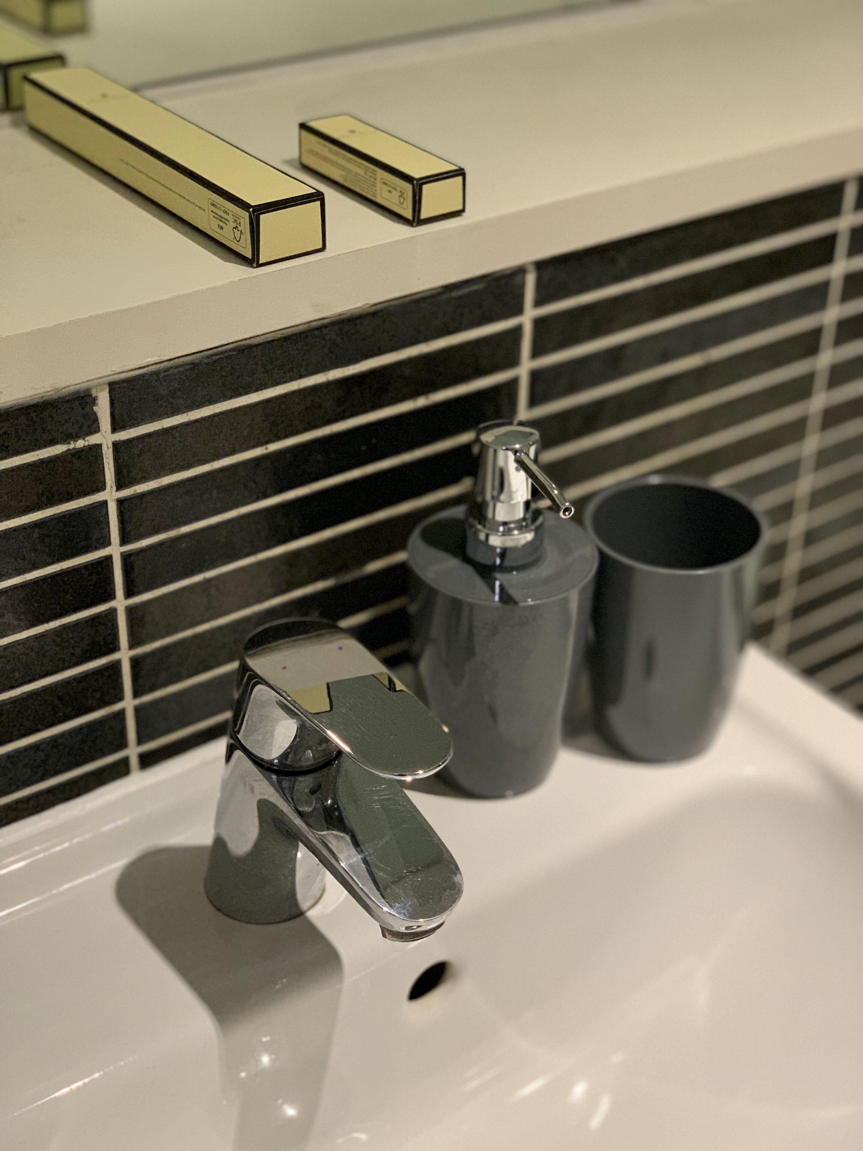 A bathroom sink with a chrome faucet, a gray soap dispenser, and a gray cup.