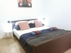 A neatly made bed with a brown headboard, two pillows, and a blanket. There is a small white table beside the bed. - Perello Old Town (Split)