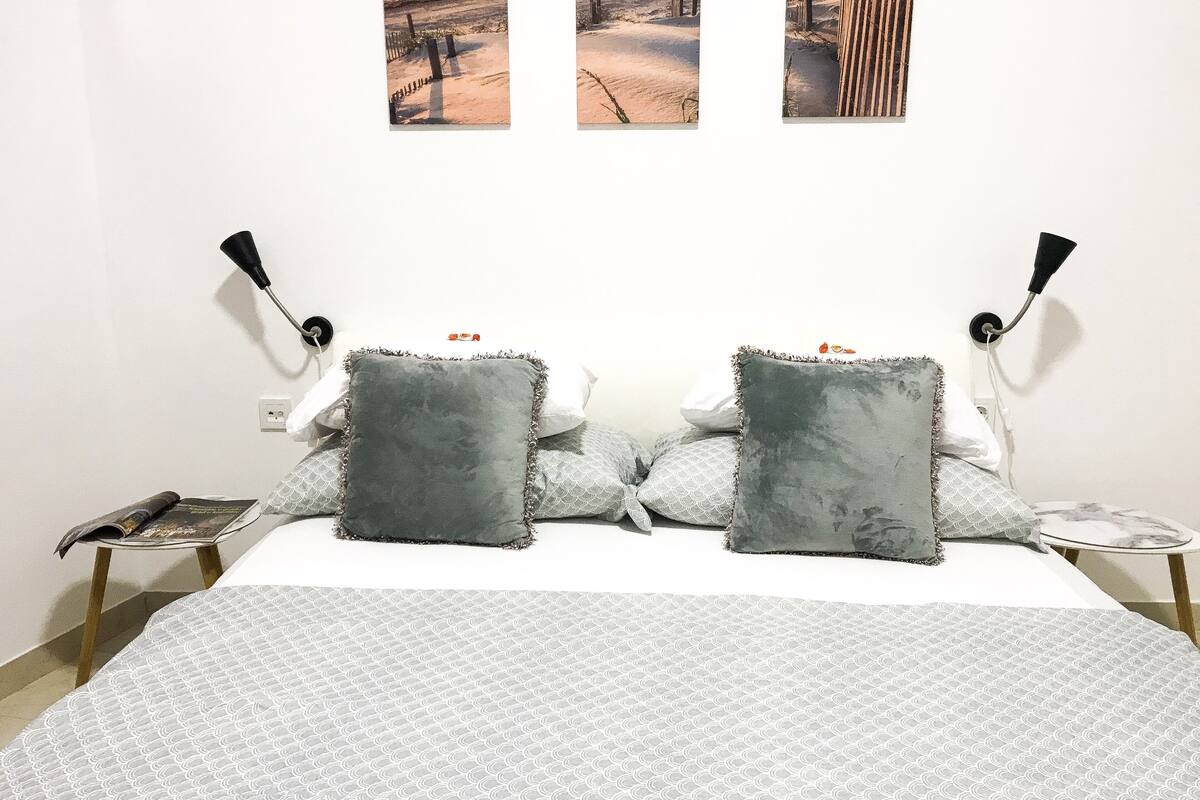 A neatly made bed with grey and white patterned bedding, two grey pillows, and a small bedside table with a lamp.