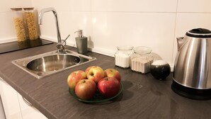 Una encimera de cocina con un fregadero, dos frascos de pasta, un hervidor y un bol de manzanas.