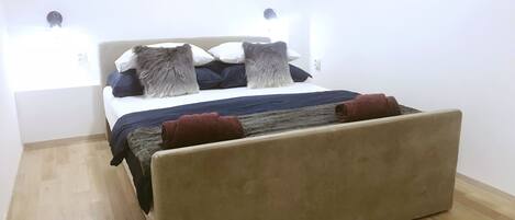 A bedroom with a bed, a headboard, a wall-mounted picture, and a light fixture.