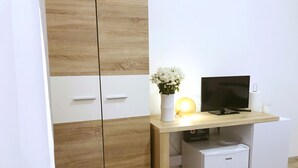 Una habitación moderna con un armario de madera, un escritorio con ordenador, un refrigerador pequeño y un florero con flores.