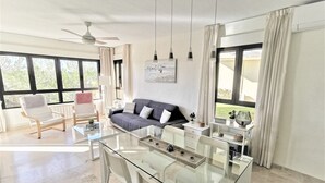Een moderne woonkamer met een glazen eettafel, een bank en een plafondventilator.
