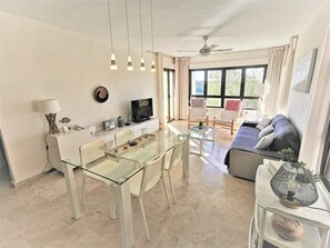 Un salon moderne avec une table à manger en verre, des chaises blanches, un canapé et un téléviseur.