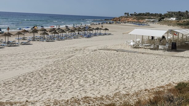 Een strand met rijen ligbedden en parasols, een restaurant aan het strand en uitzicht op de oceaan.